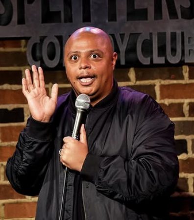Comedian with a microphone on stage in front of a brick wall